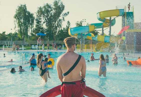 This image shows people in the swimming pool while a life guard is watching them.
